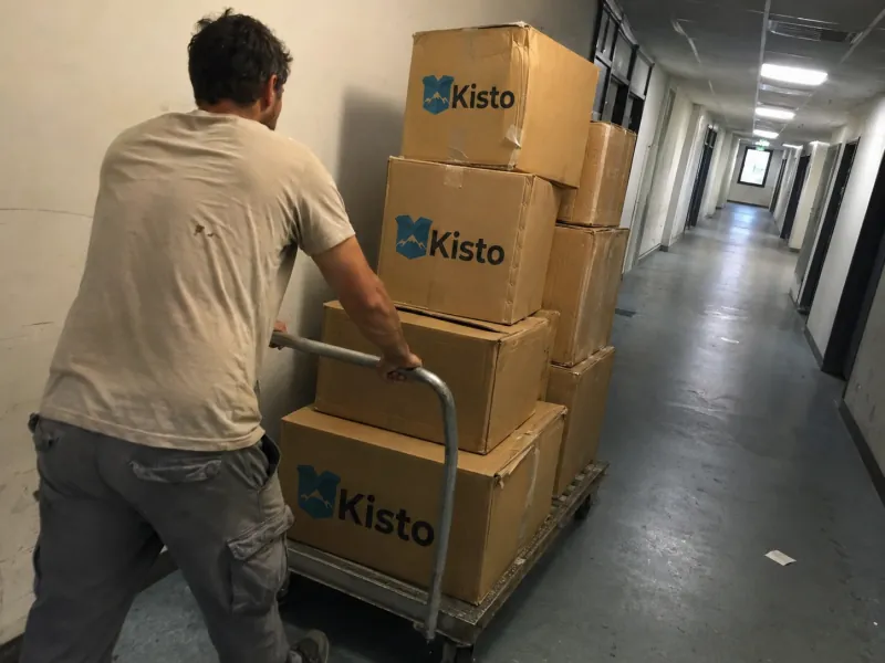 Mitarbeiter transportiert einen hohen Stapel beschrifteter Kartons durch einen Bürokorridor beim Firmenumzug