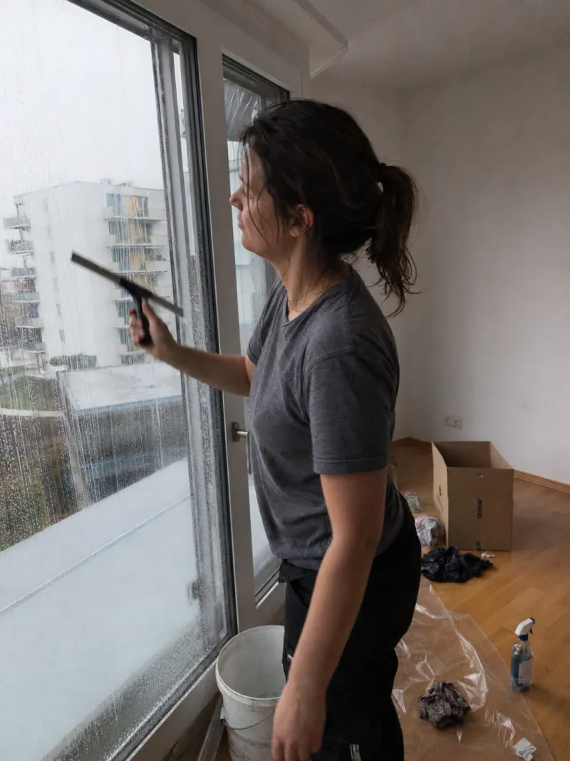 Frau reinigt mit einem Abzieher ein grosses Fenster vor der Wohnungsübergabe – Umzugsreinigung mit Abnahmegarantie